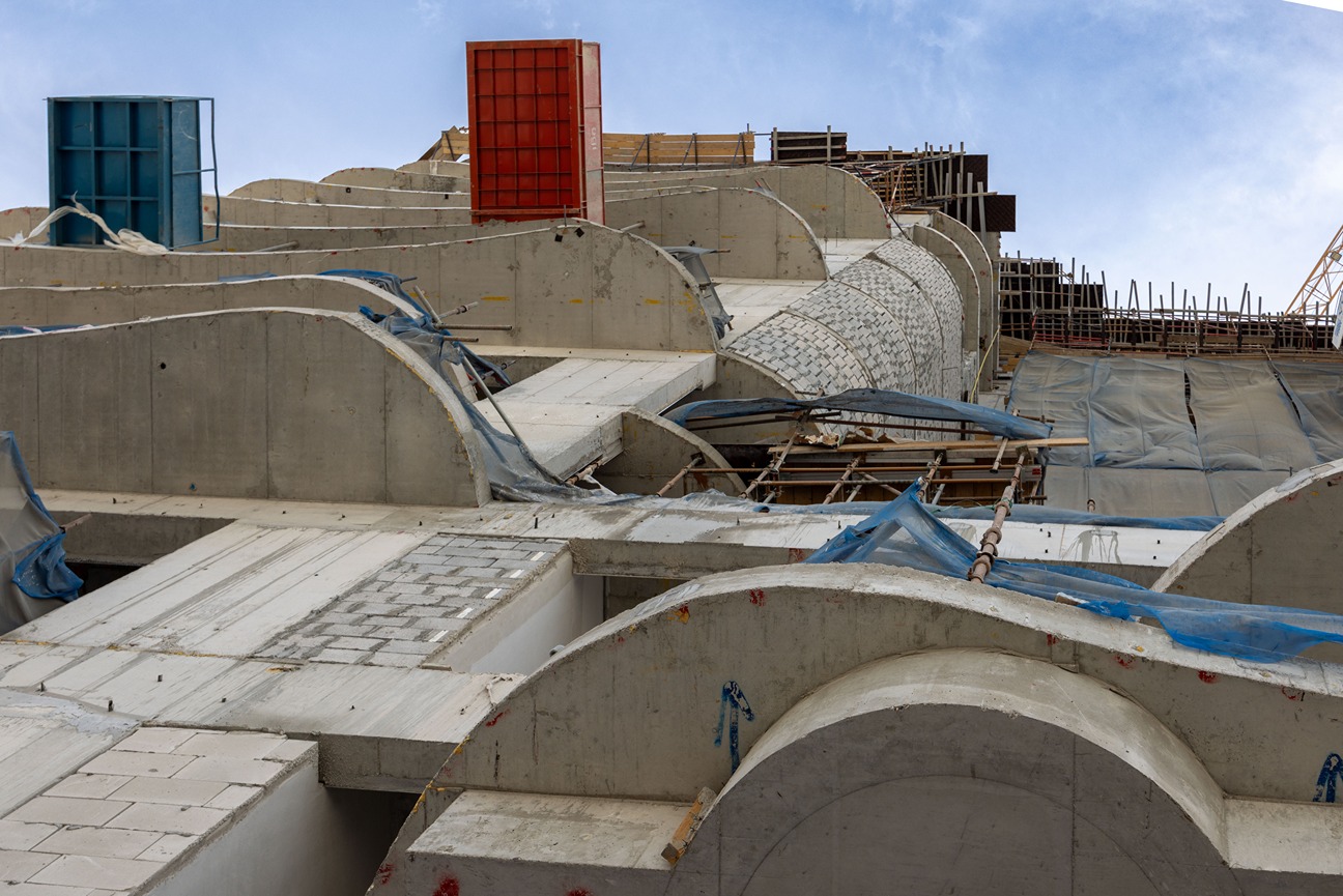 Beach Walk Residence A view of a construction site featuring concrete structures, scaffolding, and colorful formwork against a blue sky.